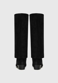 Bottes noires en daim hautes jusqu'au genou avec une forme structurée, présentant un talon bloc et des lignes épurées. Texture lisse avec un minimum de détails.