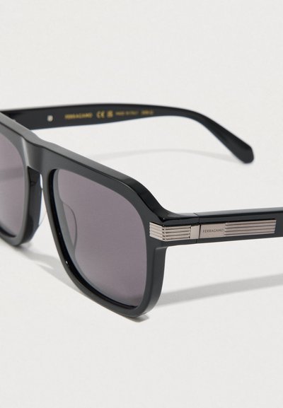 Μαύρα γυαλιά ηλίου με ορθογώνιο πλαίσιο, φακούς με γκρι απόχρωση και ασημένιες οριζόντιες λεπτομέρειες στα μπράτσα. Ομαλή υφή από πλαστικό.
