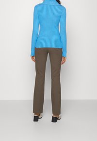 Blauer gerippter Rollkragenpullover und braune figurbetonte Hose. Der Pullover hat einen hohen Kragen; die Hose hat ein ausgestelltes Design. Glatte, leichte Texturen.