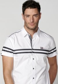 Camisa blanca de manga corta con detalles en gris, que presenta un collar tipo button-down, rayas horizontales y un logo bordado en el pecho.