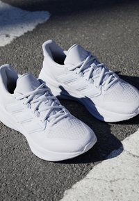 Paire de baskets blanches à lacets posée sur l'asphalte près d'une ligne de route blanche peinte sous lumière naturelle.