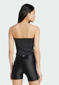 Čierny top bez ramienok v kombinácii s čiernymi lesklými šortkami s vysokým pásom. Má štýlový, hladký povrch a biele bočné pruhy.