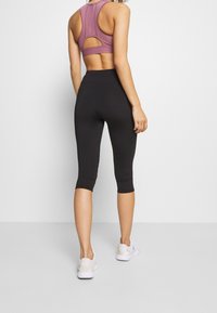 Sorte capri leggings parret med en lavendel sportsbh med udskæringsdesign på ryggen. Outfitet er kompletteret med hvide sneakers.