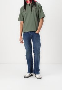 Oliivinvihreä, lyhythihainen t-paita, siniset farkut ja harmaat tennarit mustilla yksityiskohdilla, yhdistettynä punaiseen bandanaan. Yksinkertainen istuvuus ja neutraalit värit.