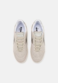 Scarpe da ginnastica beige con una trama in suede, caratterizzate da accenti grigi, lacci tondi e linguetta con marchio. Il design include dettagli di cuciture curve.