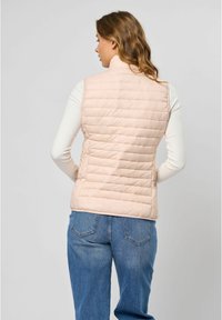 Gevoerd vest in lichtroze, met een hoge kraag, horizontaal gestikt patroon en een getailleerd silhouet. Draag het over een wit shirt met lange mouwen.