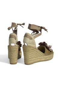 Keil-espadrilles mit beigem Textiloberteil, gewebter Jutemittelsohle, braunem Blumenakzent und verstellbaren Bändchen um den Knöchel.