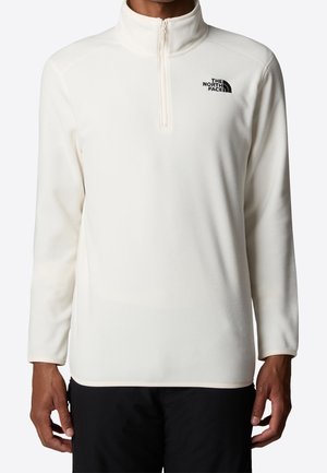 Hvid fleece pullover med lange ærmer med kvart lynlås og The North Face-logo på øverste venstre bryst, båret med sorte bukser.