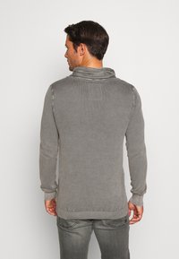 Grauer Strickpullover mit strukturiertem Muster, hoher Kragen und gerippten Bündchen. Einfaches Design, taillierte Form und lässiger Stil.
