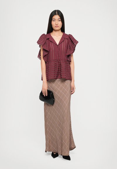 Bordeaux gestreepte blouse met gerimpelde mouwen, knoopsluiting aan de voorkant; lange bruine rok met een diagonale ruitpatroon; houdt een zwarte clutch met krokodillenstructuur vast.