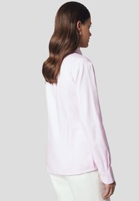 Jasnoróżowa koszula z długim rękawem o dopasowanym kroju, z zapięciem na guziki przy mankietach i delikatnym połyskiem. Gładka tkanina z klasycznym kołnierzykiem.