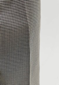 Motif de tissu pied-de-poule noir et blanc sur une surface courbée sur fond gris clair uni.