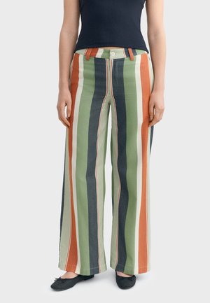 Personne portant un pantalon taille haute à jambes larges avec des rayures verticales vertes, orange, crème et bleu marine, assorti à des ballerines noires.