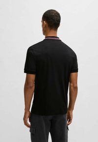 Svart polo-shirt med en kontrasterande rosa krage, korta ärmar och en slim fit-design. Slät textur och minimal branding på sidan.