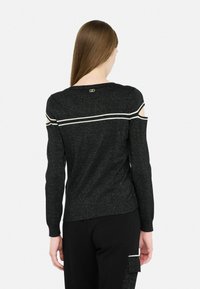 Czarna sweter z dzianiny z wycięciami na ramionach, białymi paskami na plecach oraz małym logo w okolicy dekoltu. Miękka, fakturowana tkanina.