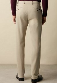 Beżowe spodnie w fasonie dopasowanym o gładkiej fakturze. Cechuje je dwa tylne kieszenie, subtelne przeszycia oraz prosty krój nogawki.