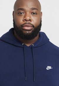 Felpa navy blue Nike in morbido pile con cappuccio regolabile e piccolo logo Nike bianco sul petto. Finitura in tessuto texturizzato.