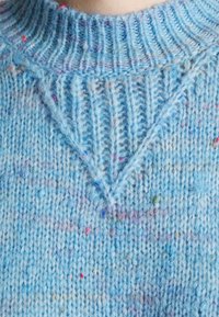 Gros plan sur un pull bleu en tricot avec un col côtelé et un motif en tricot texturé en forme de V sur la poitrine.