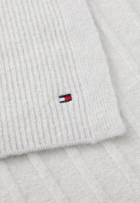 Pulover alb din tricot cu textură moale, având un mic logo brodat în roșu, alb și albastru pe margine.