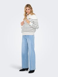 Weiß gestreifter Kapuzenpullover mit Herz-Akzent, kombiniert mit hellblauen, weit geschnittenen Jeans und schwarzen Schuhen mit Absatz. Glatter Stoff, entspannte Passform.