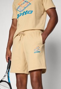 Conjunto de t-shirt e calções de algodão bege com um design gráfico em azul e laranja. Os calções têm uma cintura elástica e bolsos laterais.