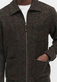 Brązowa kurtka z mieszanki wełny z zapięciem na zamek, spiczastym kołnierzem, dwiema przednimi kieszeniami i subtelną teksturą. Casualowy design w nowoczesnym kroju.