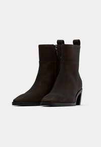 Bordo sem suede gležnjarji z koničastim nosom, zadrgo ob strani in debelim črnim peto. Gladka tekstura z minimalnimi detajli.