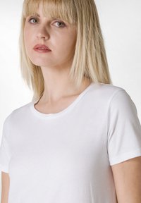 Camiseta blanca de algodón con cuello redondo y mangas cortas, que presenta una textura suave y un diseño clásico ajustado.