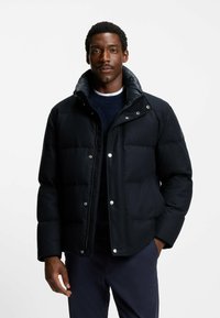 Giacca a vento imbottita in tessuto nero uniforme con colletto alto, chiusure a scatto e texture trapuntata, caratterizzata da un design elegante e accenti discreti.