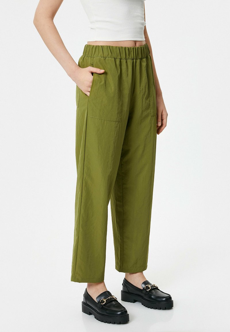 Groene, losse broek met een elastische tailleband, zijzakken en een gladde textuur, gecombineerd met zwarte platform schoenen.