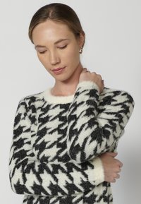Pulover cu pattern houndstooth alb-negru, fabricat dintr-un material tricotat moale, având un guler rotund și mânici pufoase.