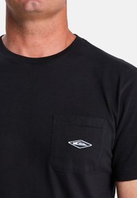 Zwarte katoenen t-shirt met ronde hals, voorzien van een borstzak aan de linkerkant en een wit geborduurd logo op de zak. Zachte textuur.