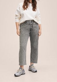 Jeans de mezclilla gris, de cintura alta, con un ajuste relajado y bajos deshilachados, combinados con un sudadera color crema y zapatillas de running grises.