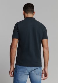 Zwart poloshirt met een klassieke kraag en korte mouwen, gemaakt van katoen, gecombineerd met lichtblauwe jeans. Glad oppervlak, minimalistisch ontwerp.