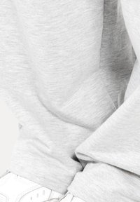 Tela de sudadera gris con una textura suave, que presenta puños sueltos y un ajuste relajado, combinada con zapatillas blancas en la esquina inferior.