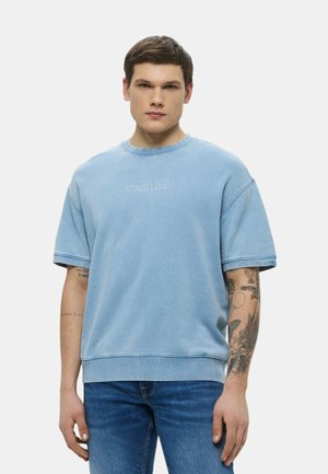 Felpa di cotone azzurro chiaro a maniche corte, con collo a costine e logo ricamato "GUESS JEANS" sul davanti. Texture liscia.