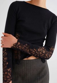 Maglietta nera a maniche lunghe con dettagli in pizzo sulle maniche, caratterizzata da un design aderente e un collo dritto, abbinata a una gonna a righe.