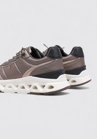 Zapatillas deportivas con parte superior de malla metálica marrón, detalles en negro y una suela gruesa blanca con recortes hexagonales. Diseño de talón redondeado.