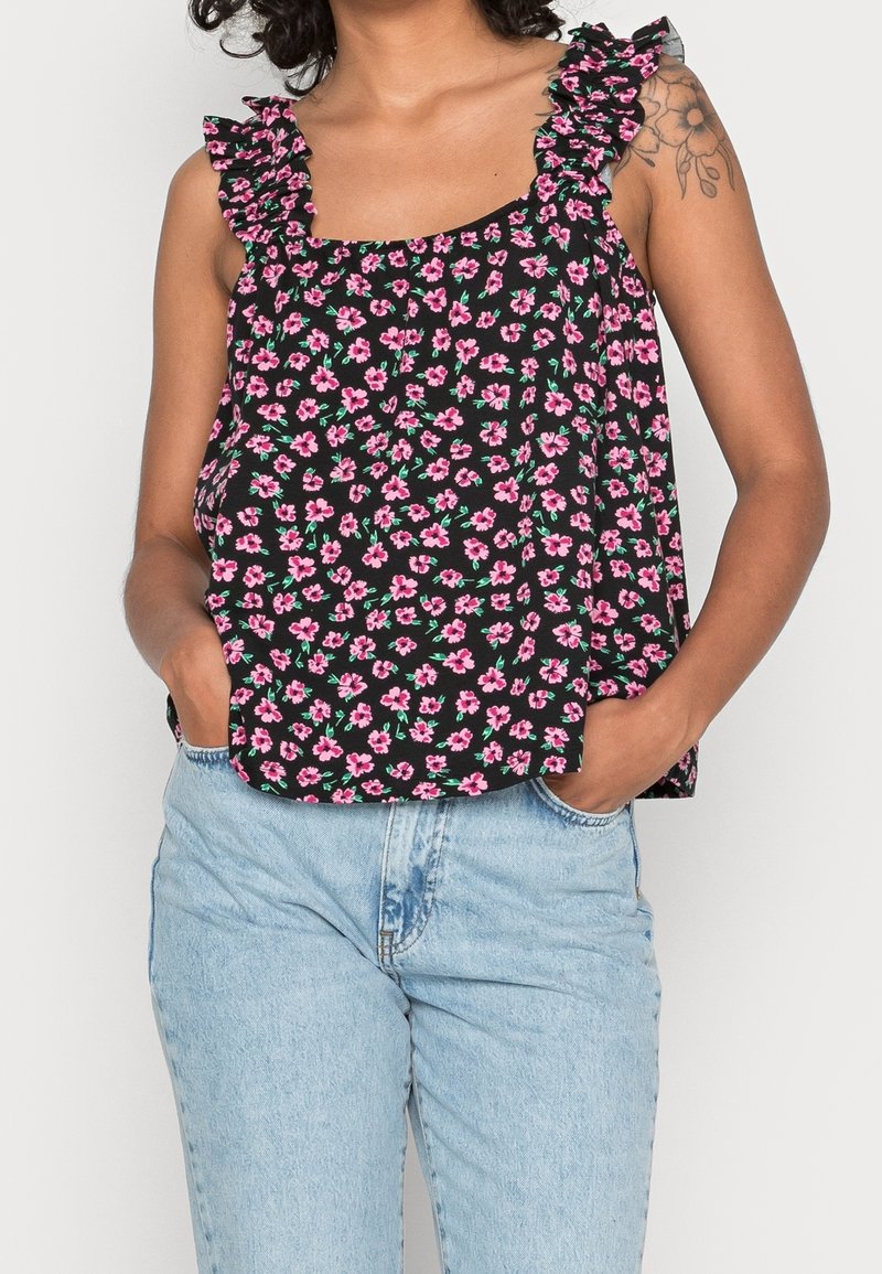 Débardeur noir à motif floral avec des fleurs roses et des feuilles vertes, doté de bretelles volantées et d'une coupe ample. Assorti à un jean en denim bleu clair.