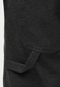 Manteau en laine gris foncé avec une poche à rabat rectangulaire et un détail de bride sur le devant.