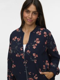 Navy bomber jacket with floral pink and green print, zip front, ribbed cuffs, and side pockets. Soft fabric with a relaxed fit.
