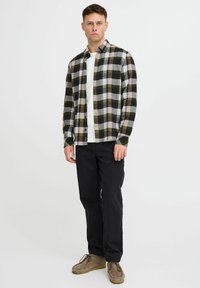 Koszula flanelowa w kratę w kolorze czarnym, szarym i oliwkowym; zapinana na guziki z długimi rękawami, w połączeniu z białym T-shirtem i czarnymi spodniami. Brązowe buty.