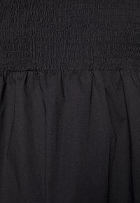 Svart tyg med elastisk shirring upptill och en rynkad, slät nederdel som skapar en texturerad kontrast.