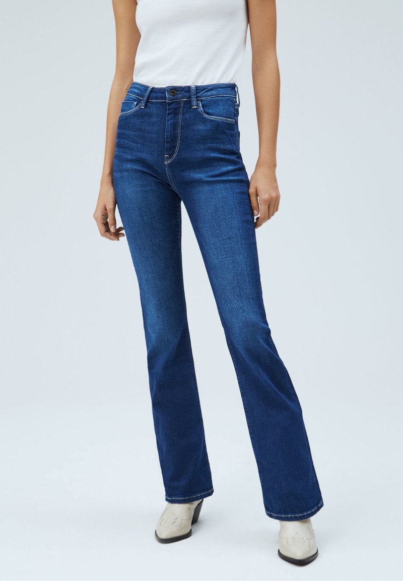 Flared Jeans aus dunkelblauem Denim, mit mittlerer Taille, fünf Taschen, weißen Nähten und Metallknopfdetails. Glatte Textur mit leichtem Stretch.