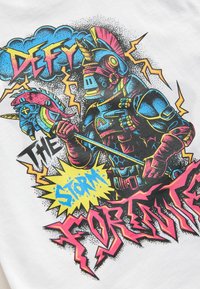 Grafisk t-shirt med en färgglad illustration av en beväpnad figur som håller ett regnbågsspeare, med fet text och blixtgrafik på vit bakgrund.