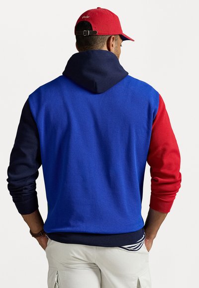 Hoodie coloré en blocs présentant des sections bleues, rouges et marine, fabriqué en tissu doux avec une poche kangourou et une capuche ajustable.