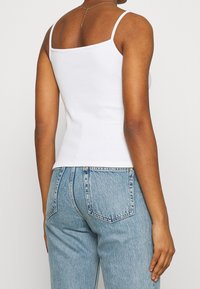 Vit figursydd linne med smala axelremmar, i bomullsmaterial, fyrkantig halsringning och en slät textur, tillsammans med ljusblå högmidjade jeans.