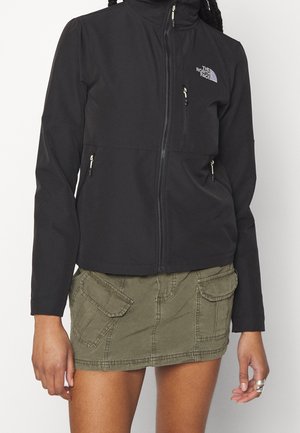 Kobieta ubrana w czarną kurtkę North Face z zamkiem błyskawicznym oraz oliwkową mini spódniczkę typu cargo z przednimi kieszeniami.