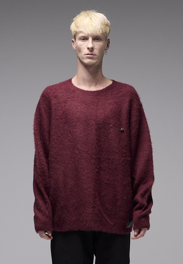 Μπορντό, φαρδύ πουλόβερ με αφράτη υφή, φαρδιά λαιμόκοψη και διακοσμητική παραμάνα μπροστά; συνδυασμένο με μαύρο παντελόνι.