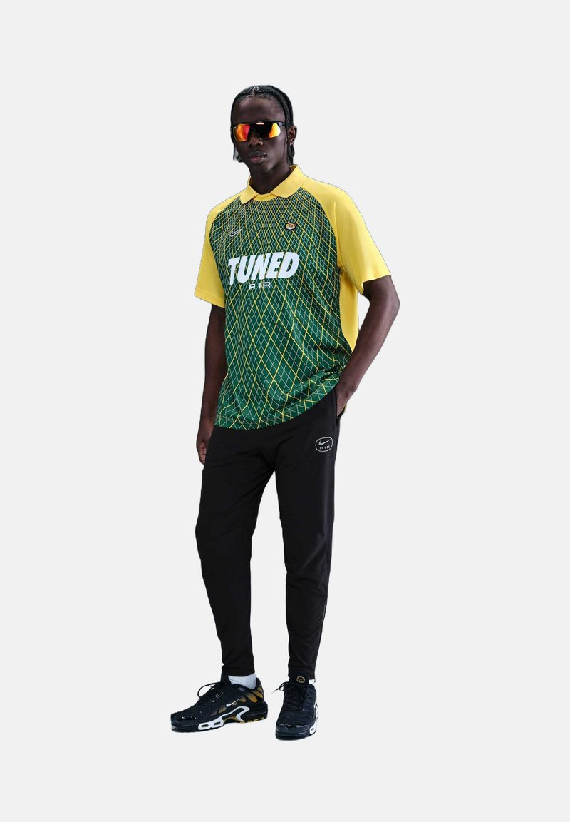 Maillot de sport avec des manches jaunes et un corps vert présentant un motif en grille ; pantalon noir et chaussures de sport noires, blanches et dorées.